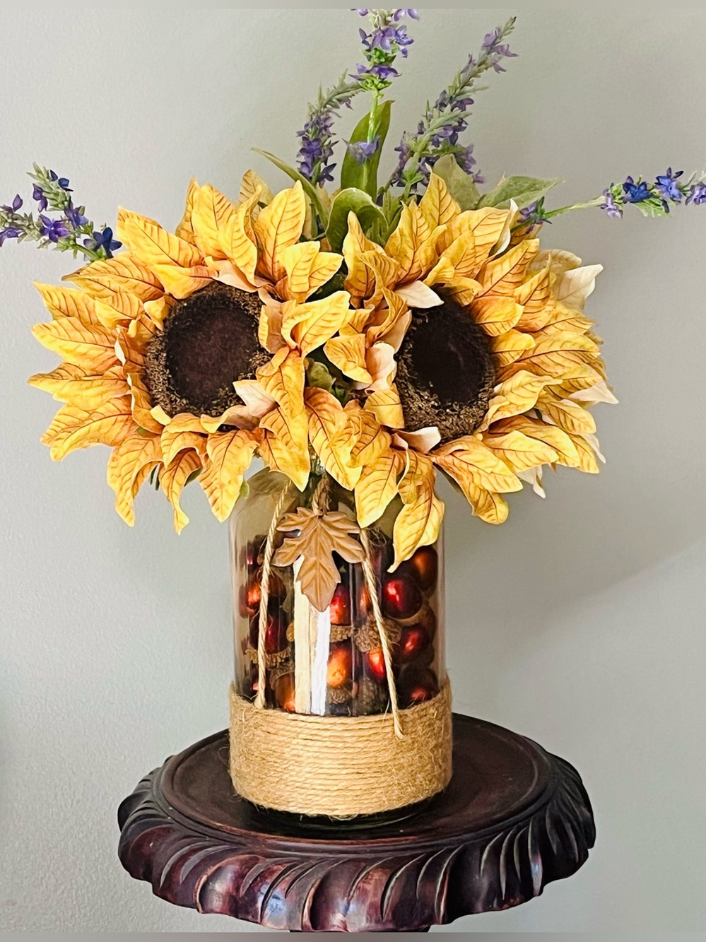 Fall arrangement with sunflowers and lavender in glass vase filled with acorns